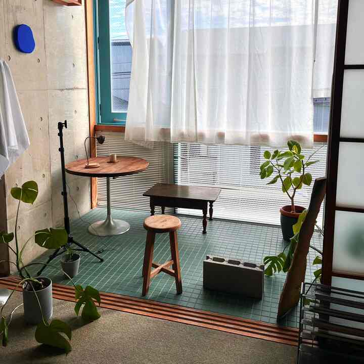 ナチュラルな色調の小さなダイニングスペース、植物とスツール、カーテンが配置された雰囲気のあるカフェ風インテリア