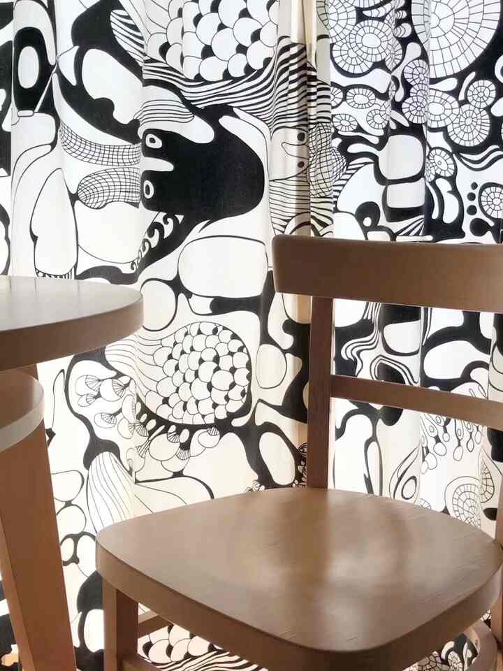 Natural wood chair and table with black and white patterned curtain in a cozy small room interior