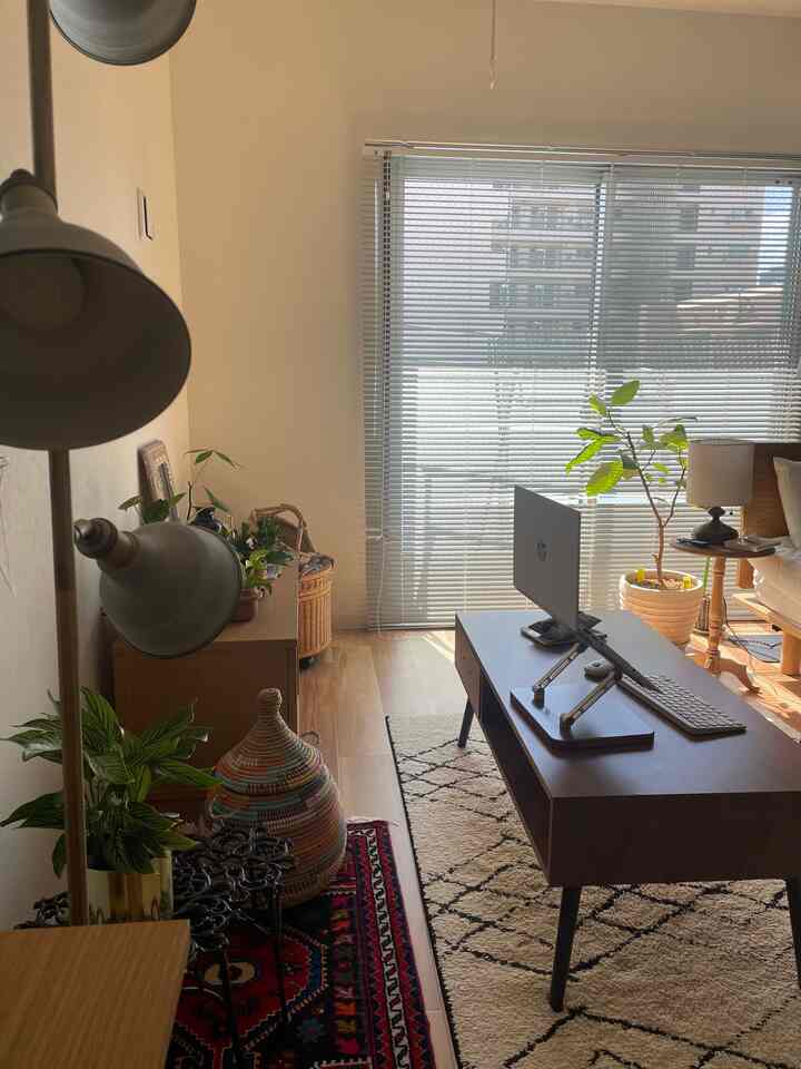 温かみのある木目調とボヘミアンスタイルの一人暮らし用ホームオフィス空間、広い窓と多様な植物が配置された居心地の良い部屋