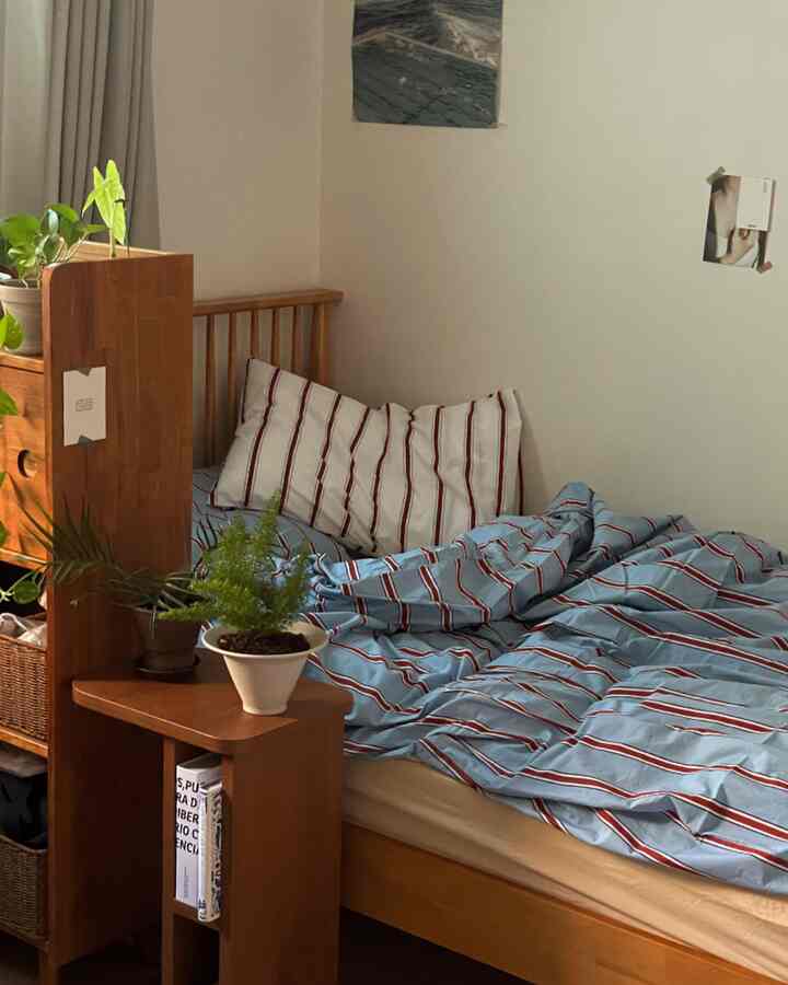 木目調とナチュラルカラーの寝室、木製ベッドに青のストライプ羽毛布団カバーと植物が配置された落ち着いたインテリア