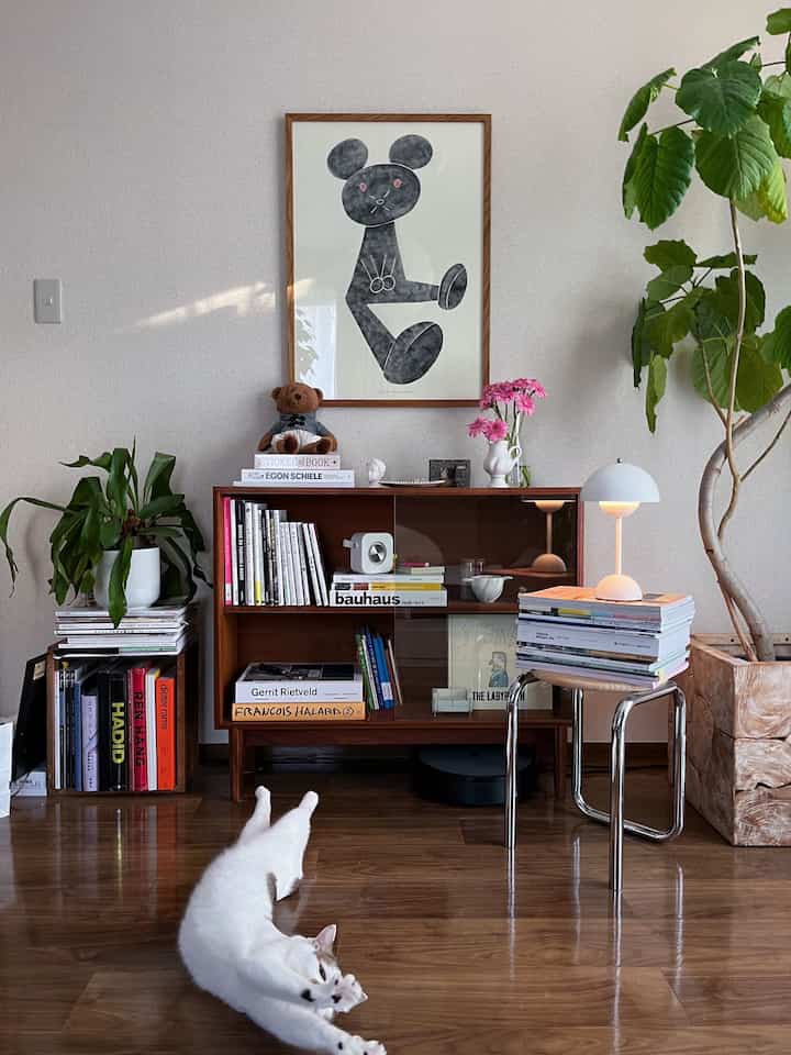 Cozy living room featuring warm wood-tone flooring, vintage furniture, a stretching cat, and lush green plants