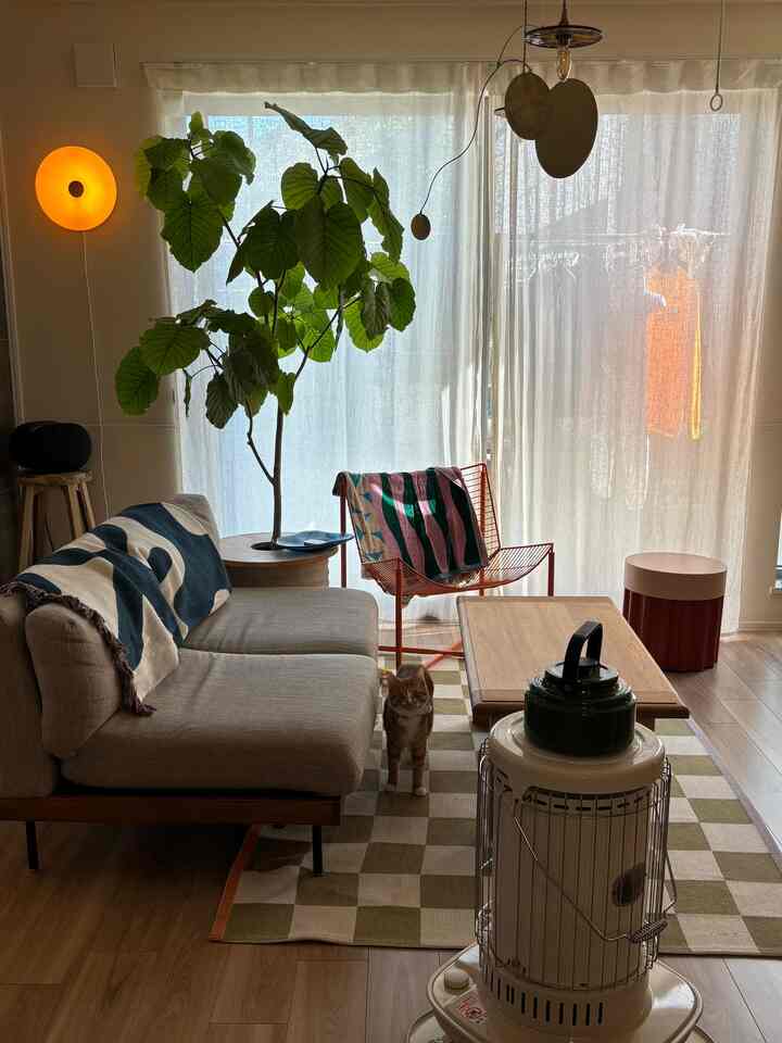 ベージュを基調とした自然な色調のリビング、観葉植物、大きなソファ、石油ストーブが配置された雰囲気のある空間