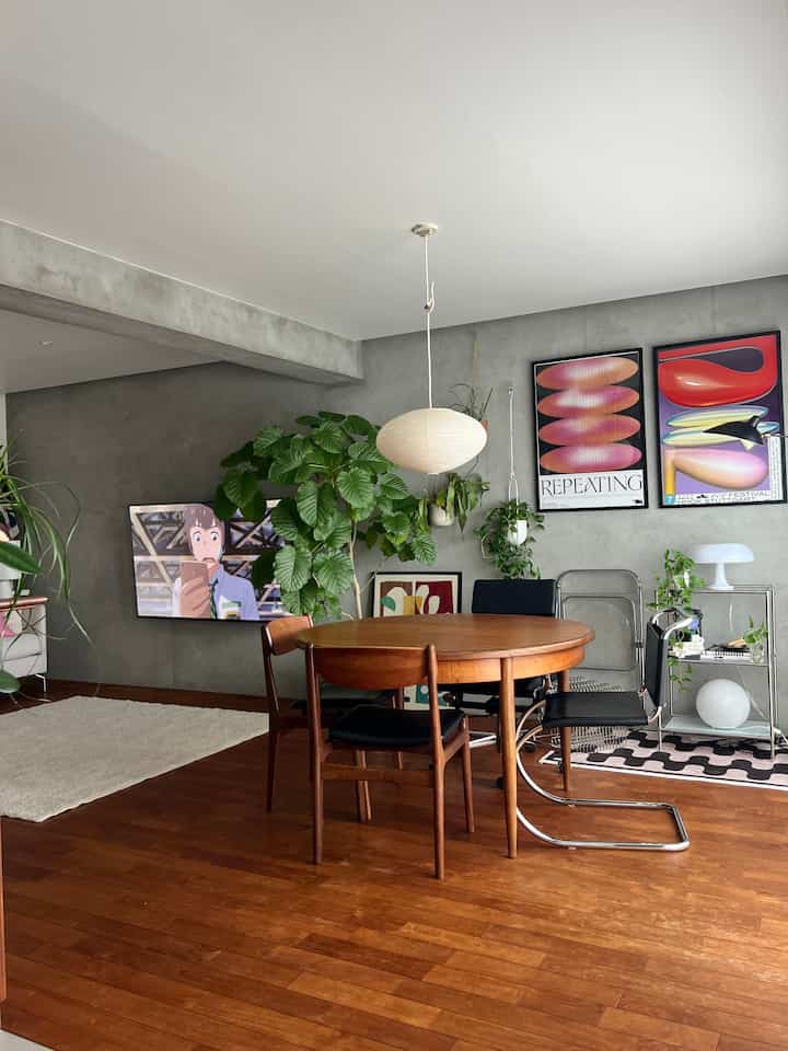 木目調とグレーの壁が映えるミッドセンチュリーモダンのダイニングルーム、丸いダイニングテーブルとカラフルなポスターが配置された印象的な空間