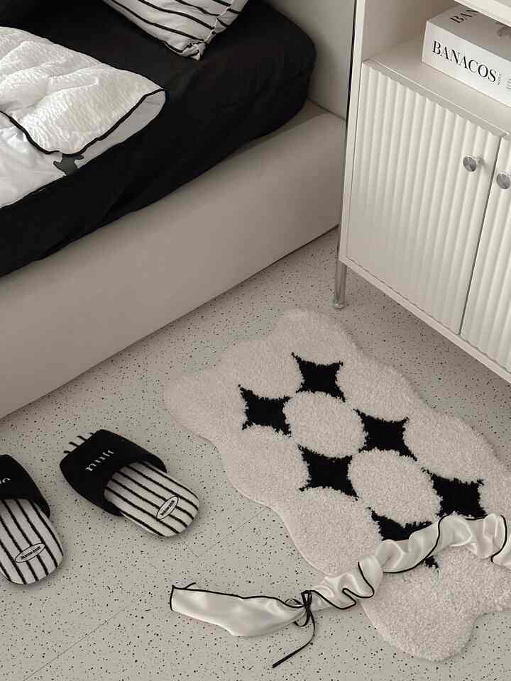 ホワイトとブラックのトーンの寝室、ベッドフレームとブラックダイヤモンド柄のラグが配置されたモダンな空間