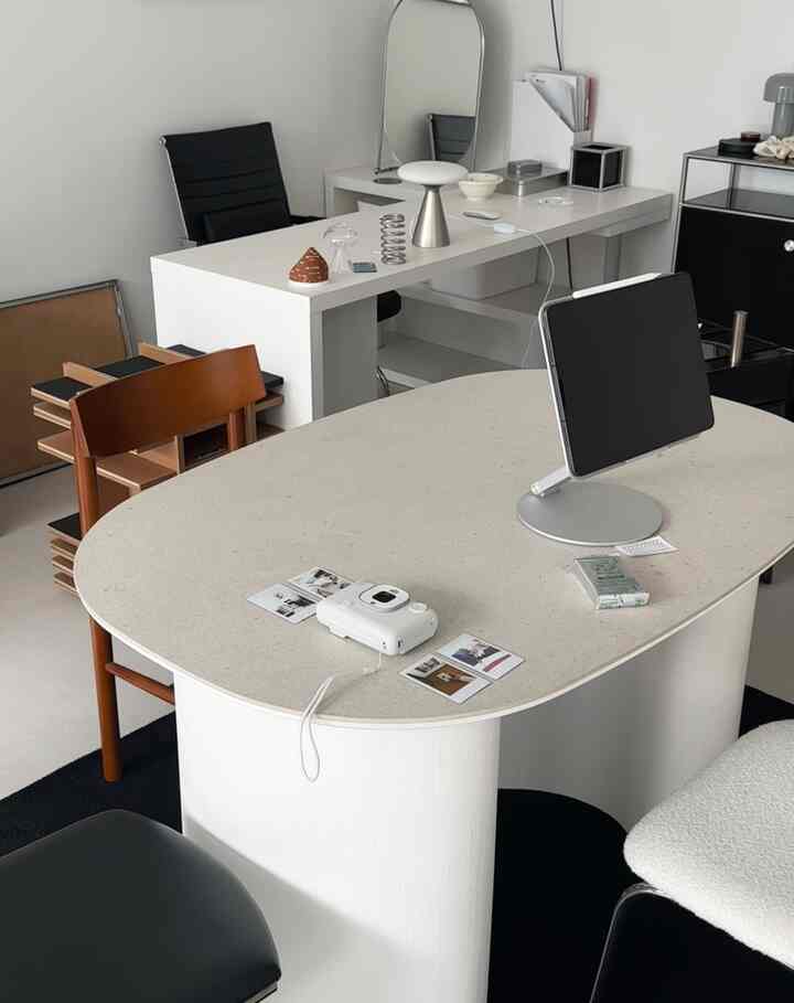 白と黒のトーンが印象的なコンパクトなホームオフィス、楕円形のテーブルにタブレットスタンドとオフィス用品が配置されたモダンなインテリア