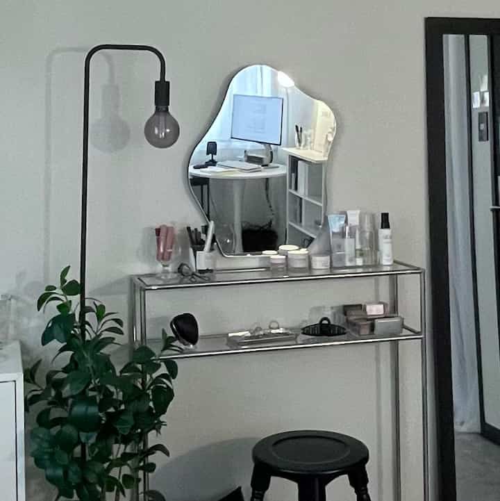 モノトーン調の玄関スペース、金属フレームのドレッサーと不規則な形の鏡、フロアランプと緑の植物が配置されたシンプルなインテリア