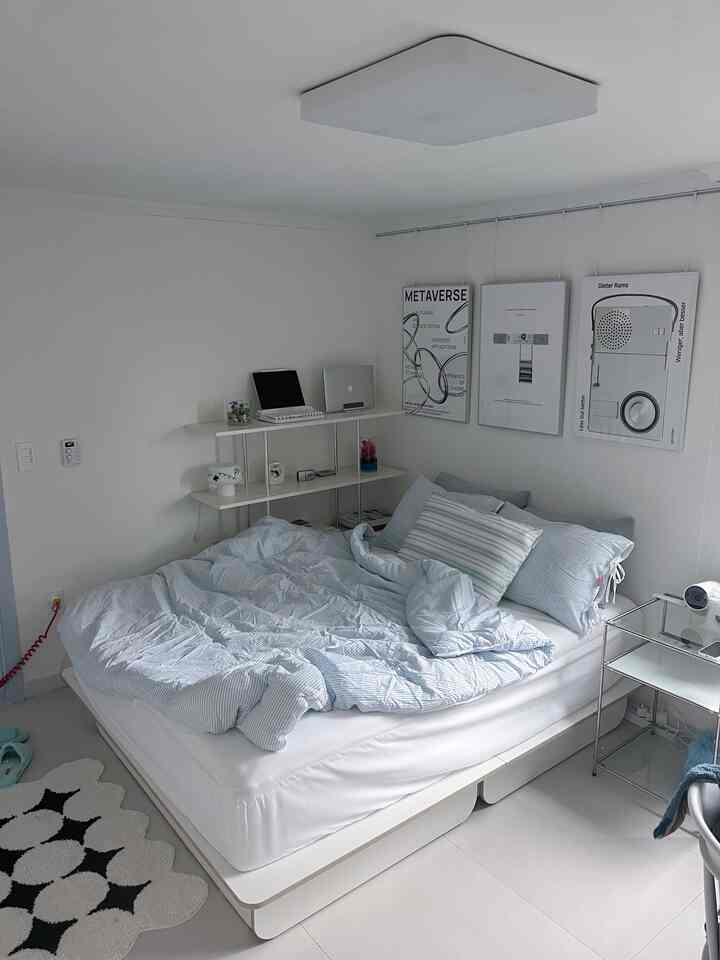 白と青の色調の寝室、収納型ベッドとストライプ柄寝具、モダンなポスターが配置された雰囲気のある小さな部屋