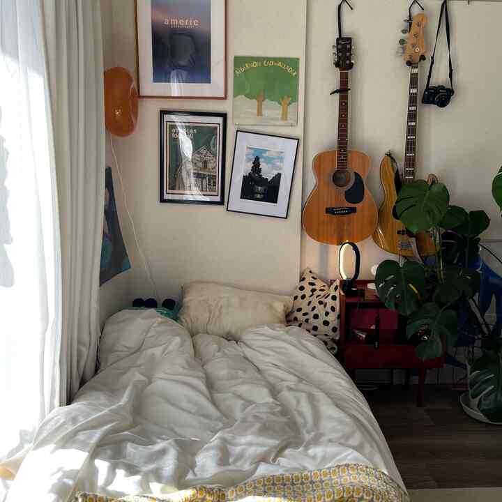 Natural-toned 8-tatami bedroom featuring a bed with pillows and cushions, framed artworks on the wall, and guitars for a cozy atmosphere