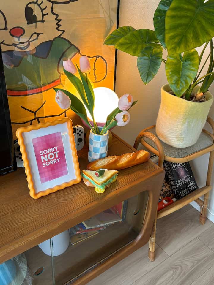 ナチュラルな木目調のリビング、カラフルな造花と植物、テーブルランプや額縁が置かれた雰囲気のあるインテリア