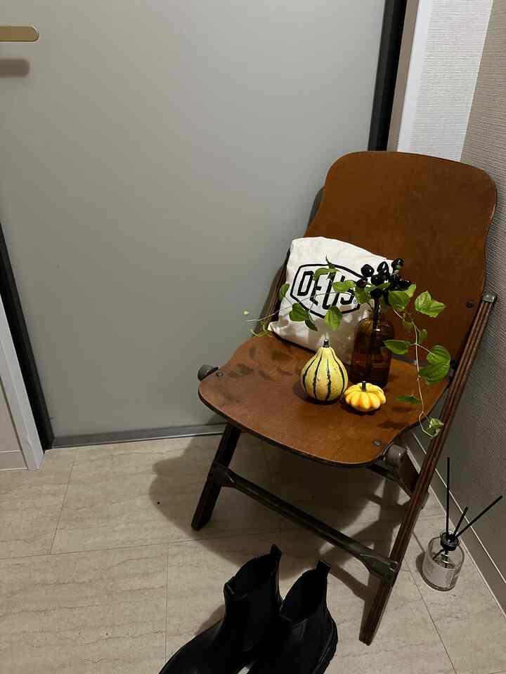 ウッドトーンとブラウンカラーの玄関、木製チェアに植物と飾りかぼちゃが置かれ、落ち着いた雰囲気のあるインテリア