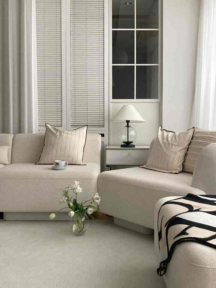 柔らかなベージュのトーンのリビング、モダンなソファとクッション、照明が配置された落ち着いた雰囲気のインテリア