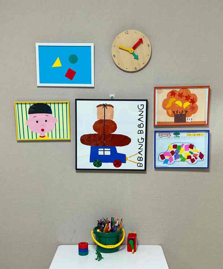 明るいホワイトテーブルの上に子どもたちが描いたカラフルな額縁とポスターが壁に飾られた子供部屋のインテリア