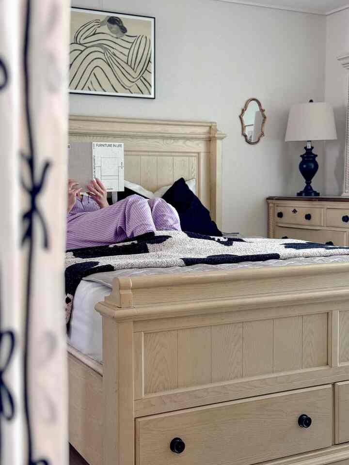 白とナチュラルカラーの寝室、中央に木製ベッドフレームと白黒のブランケットが配置された雰囲気のあるインテリア