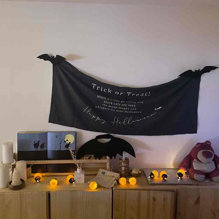 ブラックと木目調のリビング、ハロウィンインテリアとディフューザー、ピンクのぬいぐるみが配置された雰囲気のある空間