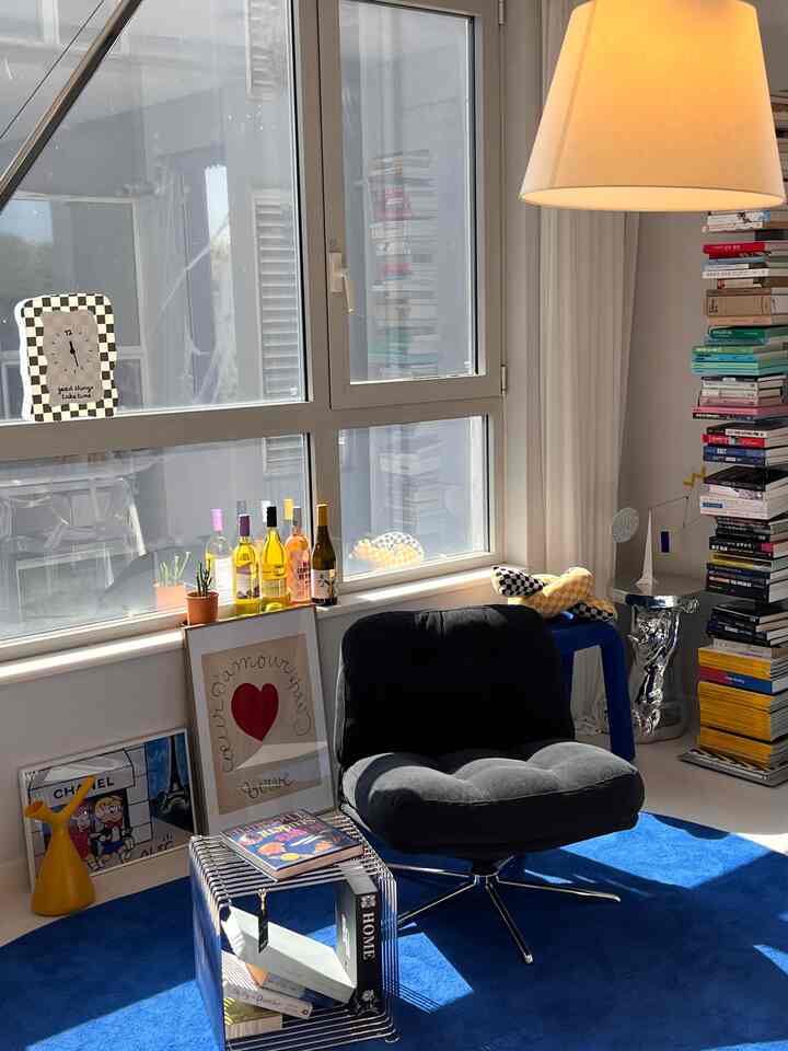 Modern study with white walls and windows, blue carpet, black armchair, transparent side table, books, and warm lighting