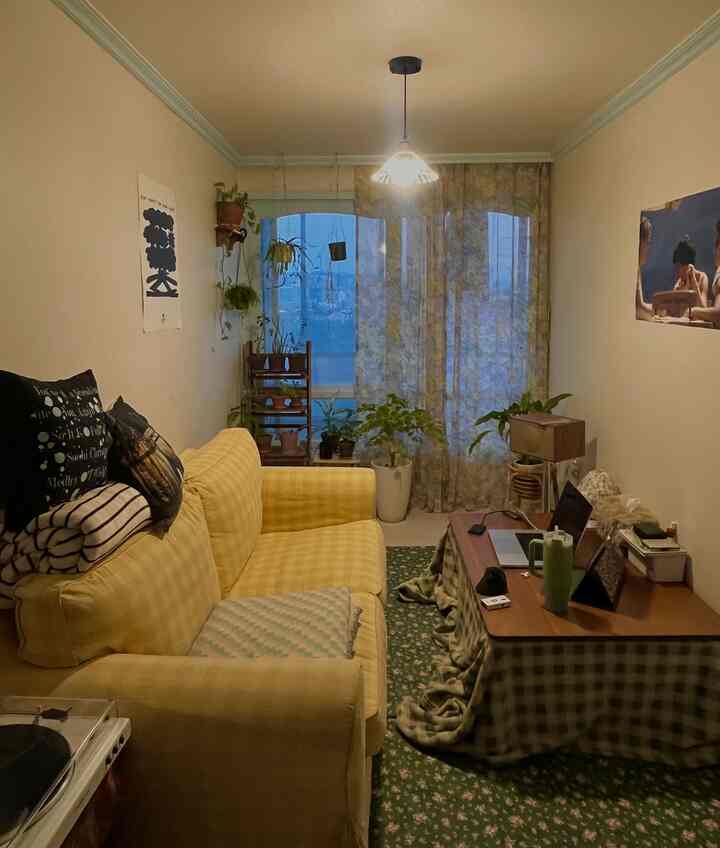 ナチュラルな色調のリビング、黄色のソファと植物、花柄のカーテン、ペンダントライトが配置された印象的な空間