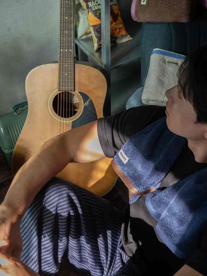 ネイビーとブラウンのタオルとギターが置かれた、陽射しが差し込む落ち着いた寝室のインテリア