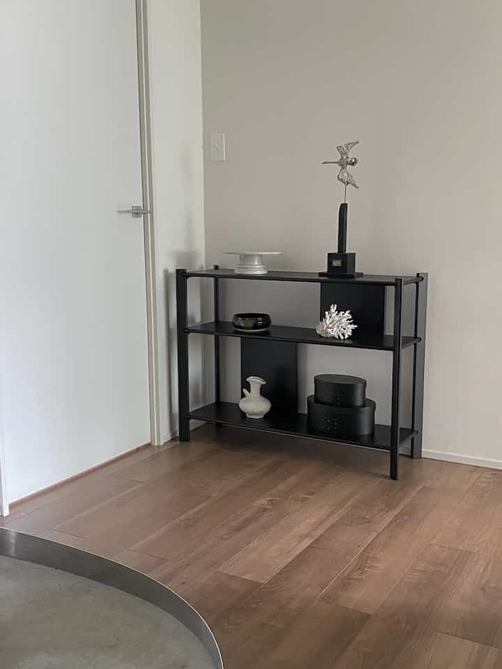 木目調の床とミニマルな装飾を備えた黒い棚が配置された印象的な玄関のインテリア