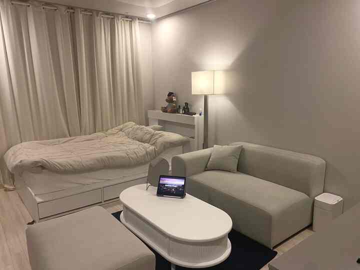 Beige and white toned 8-pyeong studio apartment featuring bed, sofa, nightstand, and floor lamp in a clean, simple atmosphere