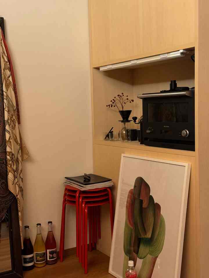 木目調のビルトインキャビネットと赤いスツールが置かれたコンパクトな1LDKのキッチンコーナー、床に立てかけられたロナン・ブールレックのアートポスター