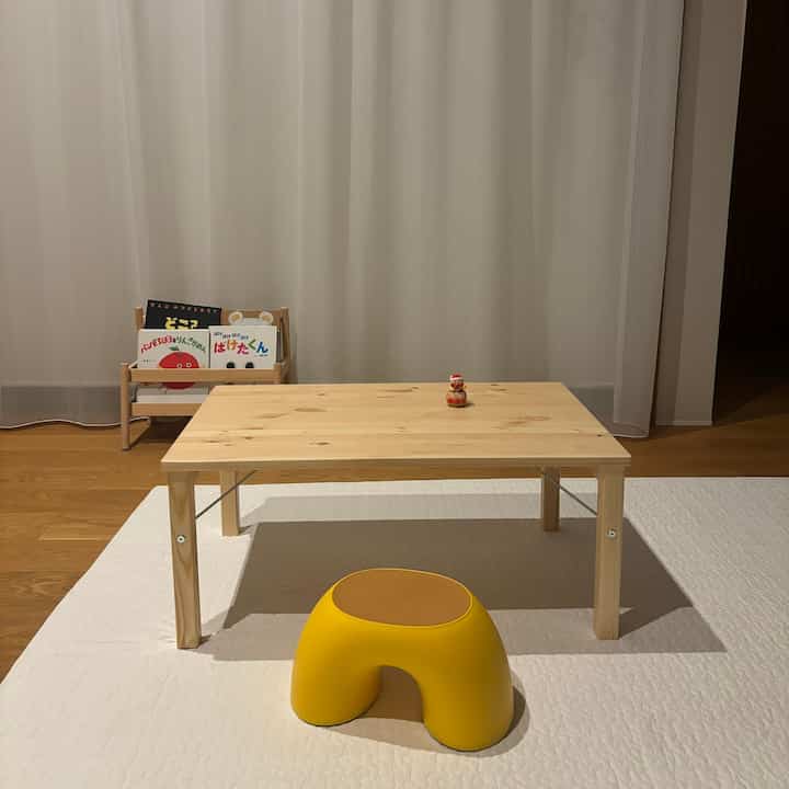 明るい木目調の子供部屋、パイン材のローテーブルと黄色いキッズスツール、子供の絵本棚が配置された温かみのある印象的な空間