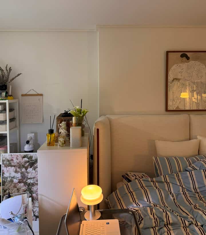 白とベージュのトーンの縦長ワンルーム寝室、ベッドと収納棚が空間の仕切りを成す雰囲気のあるインテリア