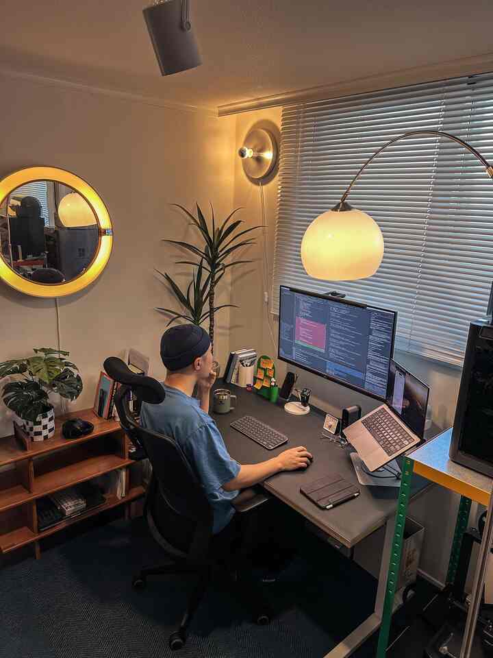 Warmly lit compact home office featuring desk, office chair, plants, and blinds creating a cozy workspace