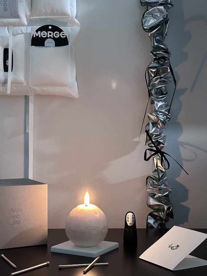 Simple space featuring a lit white spherical candle on a black table with hanging objets on the wall