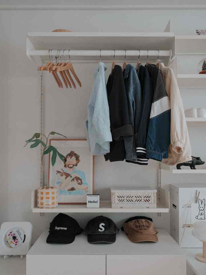 白とナチュラルカラーのウォークインクローゼット、壁棚とハンガーが配置された雰囲気のあるインテリア。