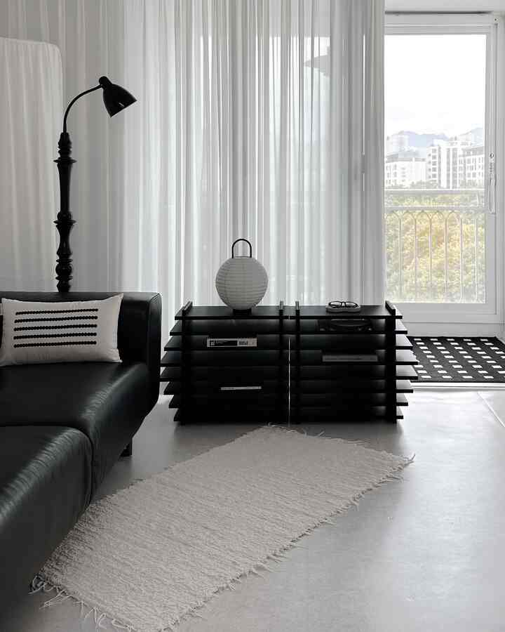 Modern living room with black sofa and floor lamp against white sheer curtains, creating a clean atmosphere