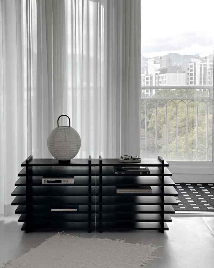 Modern living room with white and black tones, featuring a unique storage shelf and white curtains creating a cozy atmosphere