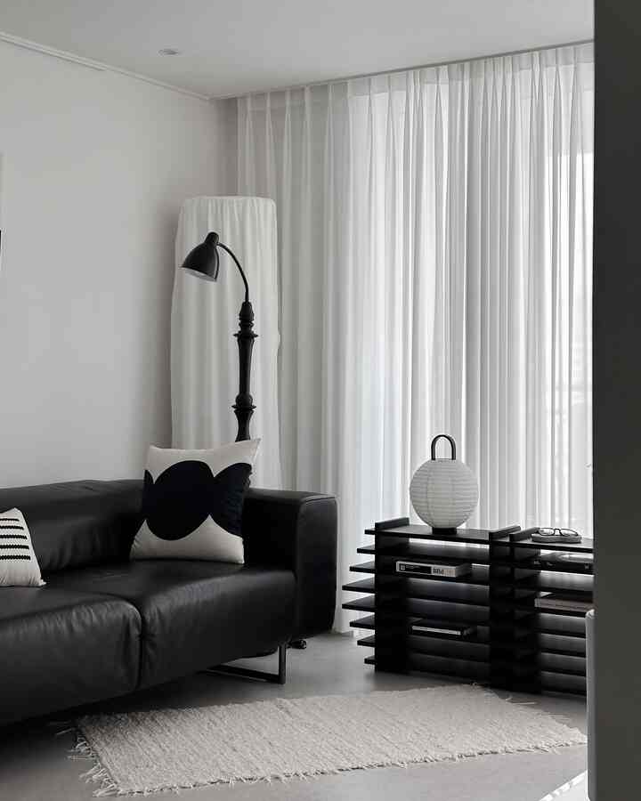 ブラックとホワイトのモノトーンリビング、黒いレザーソファと棚、白いカーテンとラグが配置されたシンプルでモダンなインテリア