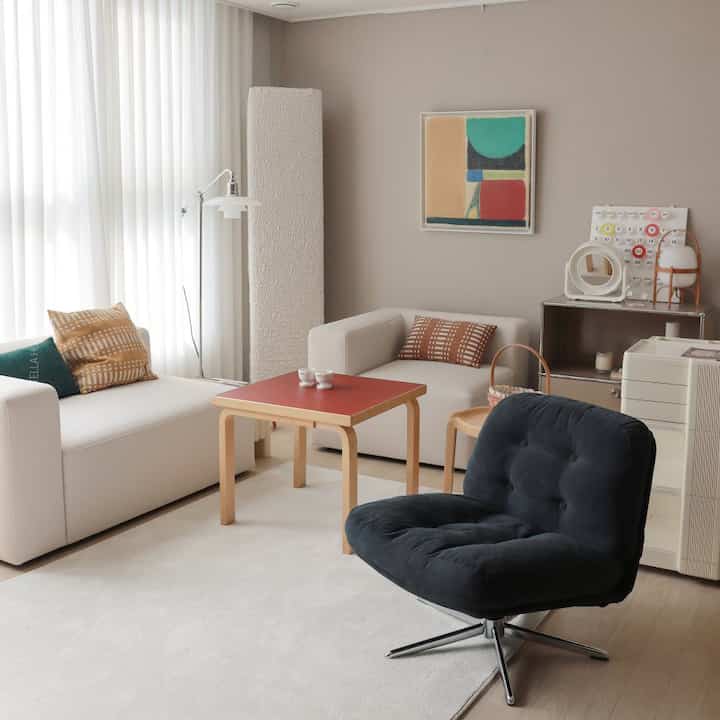 Natural-toned living room with ivory and wood elements, featuring cream sofas, a black armchair, and a reddish side table in a neat layout
