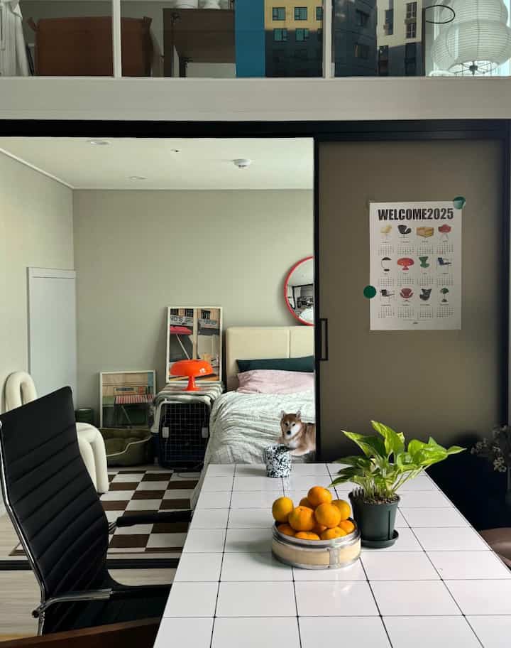 Natural-toned bedroom and home office space featuring a white tiled table with plants and oranges near a sliding veranda door, creating a cozy indoor setting