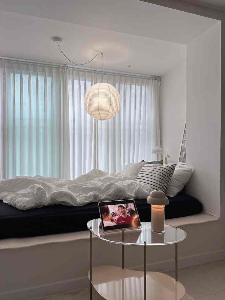 白と黒のトーンの寝室、大きな窓とカーテンの前にベッドと透明なテーブルランプが配置された落ち着いた空間
