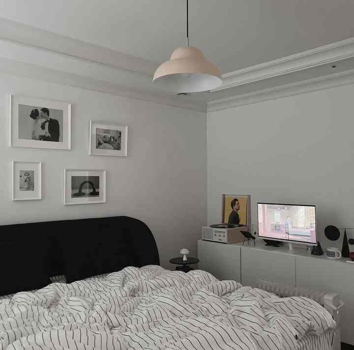 白と黒のトーンでまとめられたモダンでコンパクトな寝室、ストライプの寝具と壁のアート、テレビ台が配置された雰囲気のあるインテリア