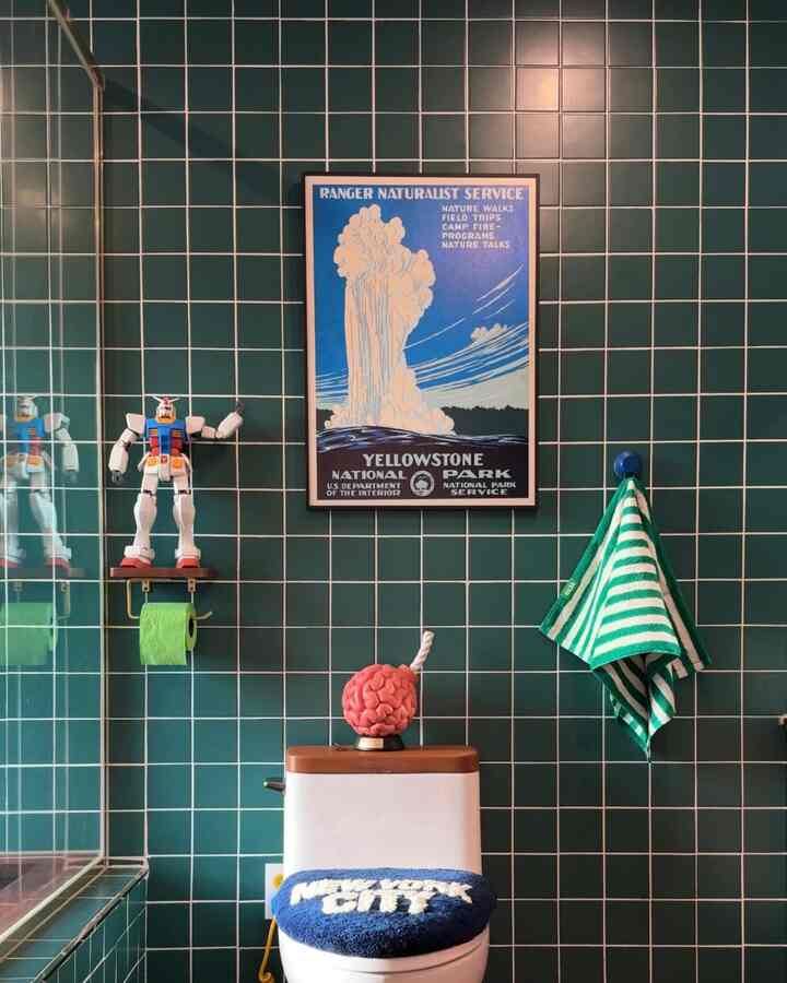 緑のタイル壁と白い便器が配されたモダンなトイレ、緑のタオルと額縁が置かれた落ち着いた雰囲気のインテリア