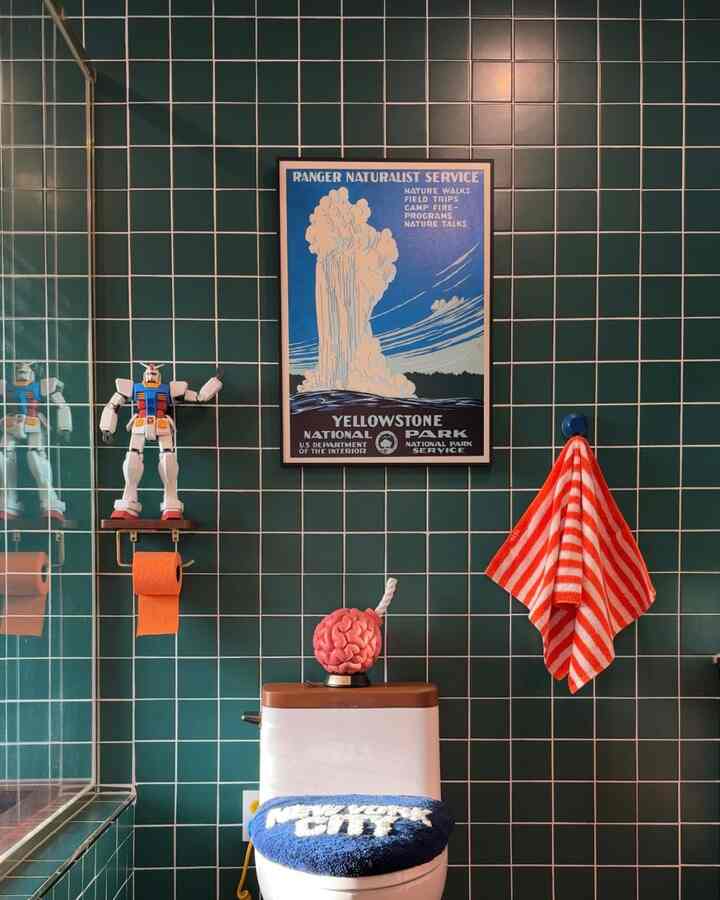 濃い緑色の壁タイルが特徴的なトイレ空間、中央に白い便器と青いトイレカバー、右側に赤と白のストライプタオルが掛けられた雰囲気のあるインテリア