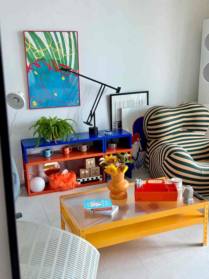 Mid-Century Modern living room featuring vivid blue and orange shelving, yellow coffee table, and striped armchair with a lively color palette