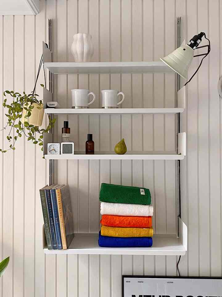 Modern bathroom storage featuring white-toned shelves with neatly stacked towels in various vibrant colors against a white paneled wall