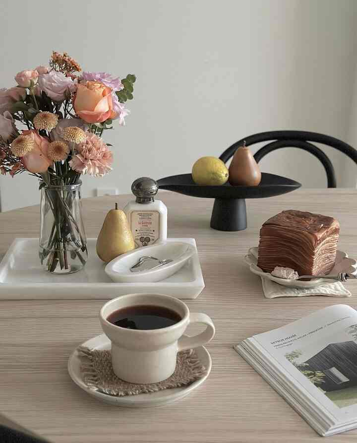 Beige-toned dining room featuring fresh pastel flower bouquet, ceramic cup, and marble trays with a natural cozy atmosphere