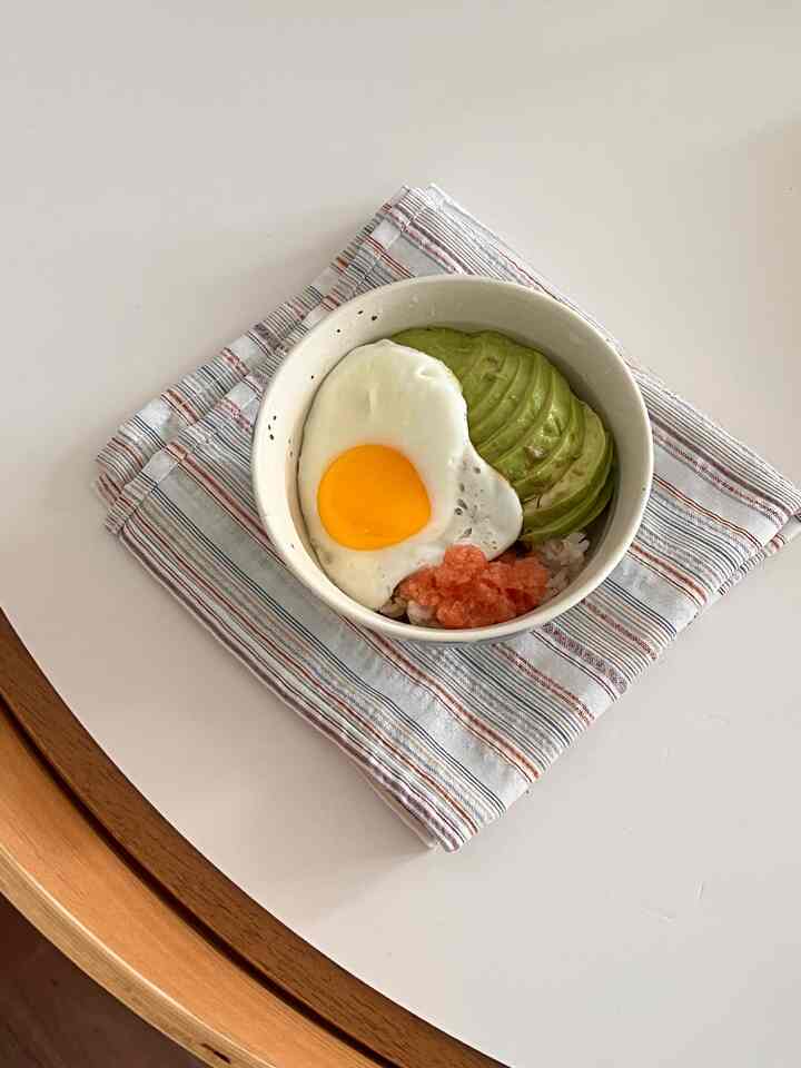 木目調と白が調和したダイニングテーブルにストライプのテーブルクロスとアボカドのせごはんが置かれたシンプルな空間