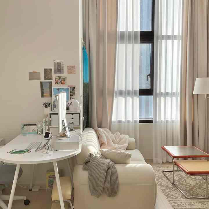 白とベージュのトーンが調和したワンルームのリビング兼ホームオフィス、ソファとコーヒーテーブルが配置された落ち着いた雰囲気のインテリア