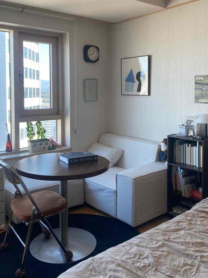 ホワイトとブラウンのトーンが特徴の狭い1Kの部屋、ソファベッドと丸テーブル、書棚が配置された居心地の良い空間