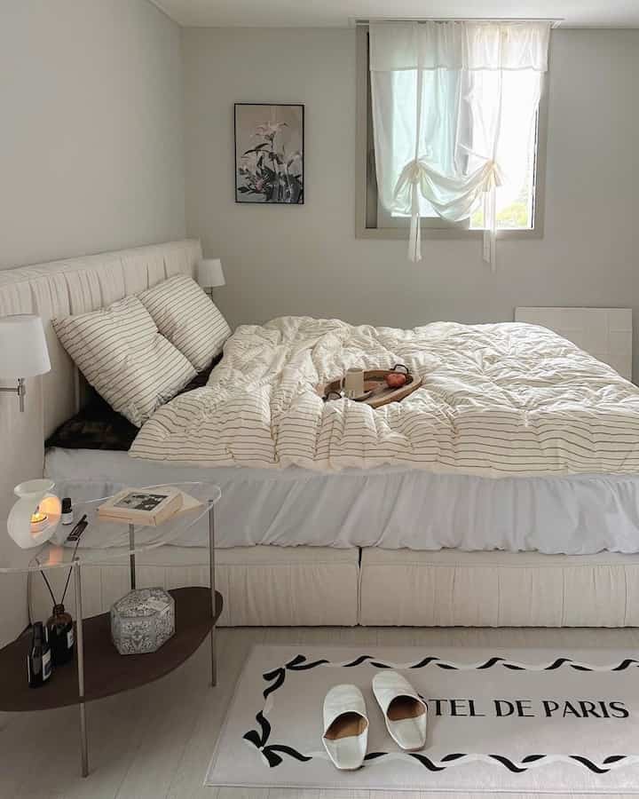 白い色調の寝室、ストライプの寝具とシンプルな家具が配置された落ち着いた印象的な空間