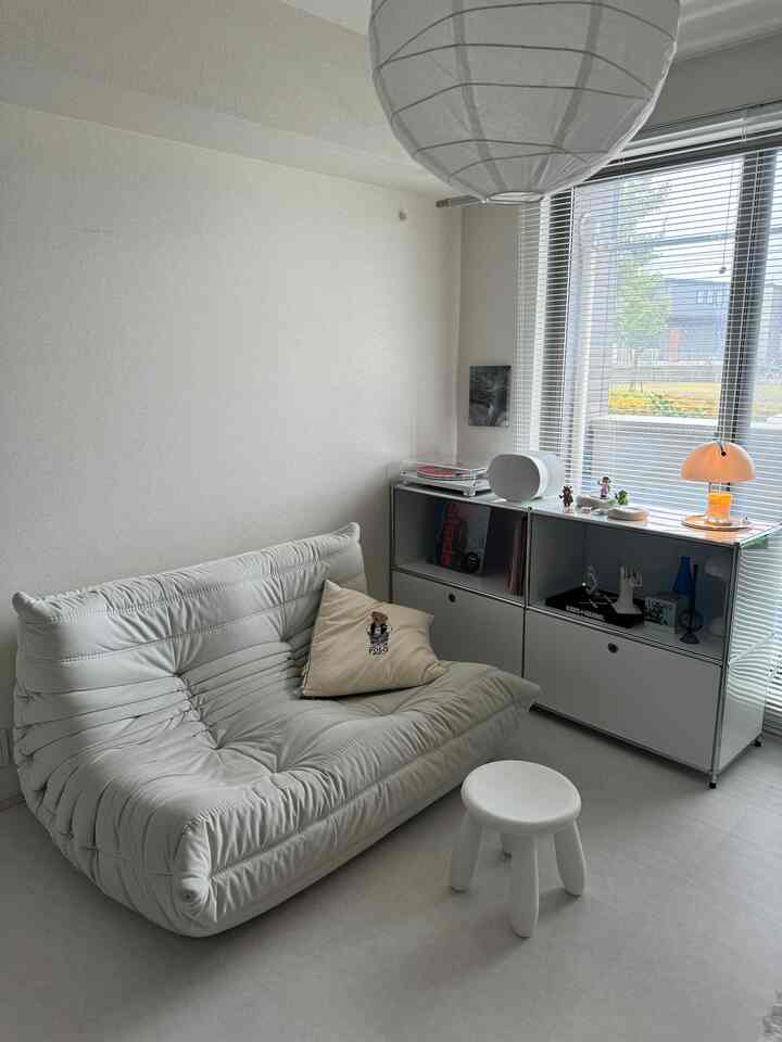 White-toned living room featuring a comfortable sofa, stool, and neat storage cabinet in a simple space