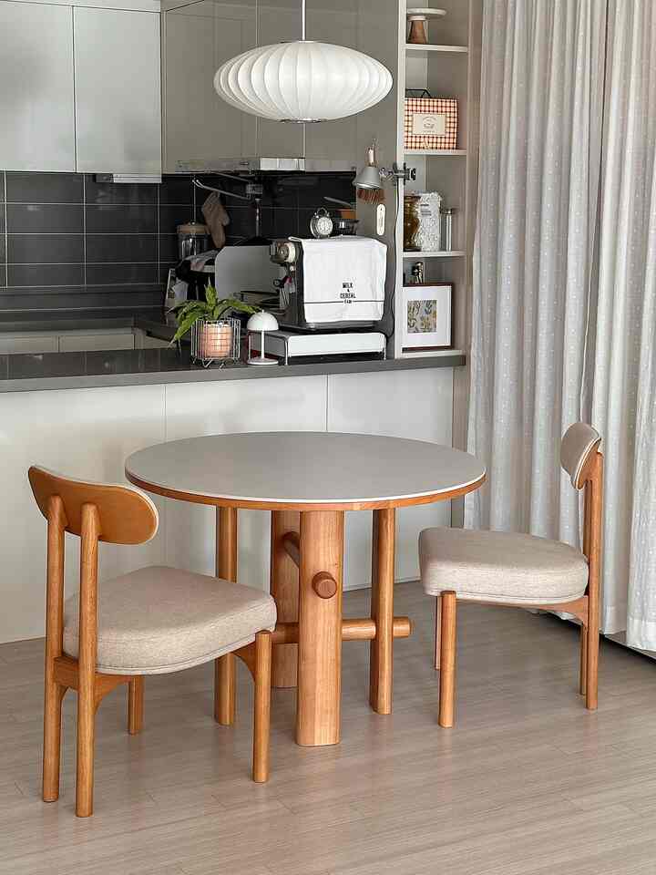 Natural color tone modern kitchen and dining area featuring a round table, pendant light, and coffee machine for two