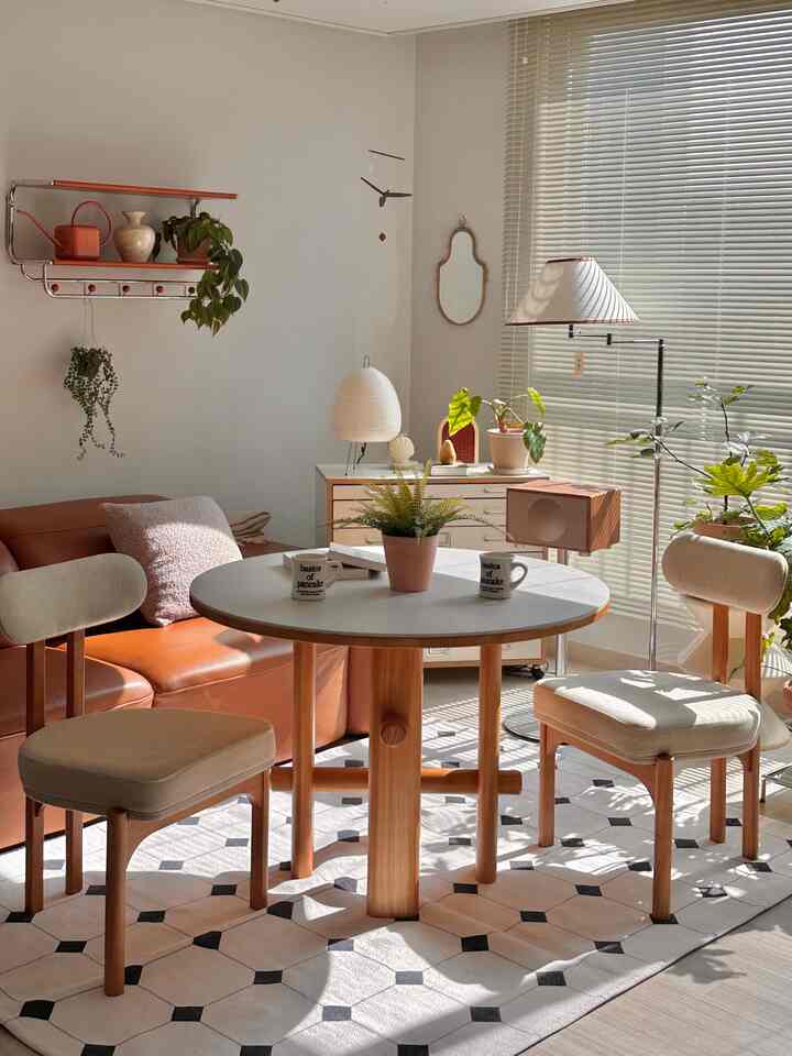 温かみのある色調のリビング兼ダイニングスペース、木製のダイニングテーブルと椅子、茶色のレザーソファ、多様な植物が配された雰囲気のあるインテリア