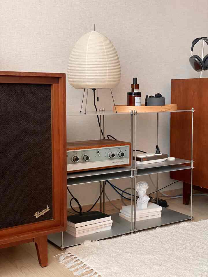 Living room with white walls and brown vintage audio equipment, featuring a white paper lantern lamp, sculpture on modern shelving, and cozy rug