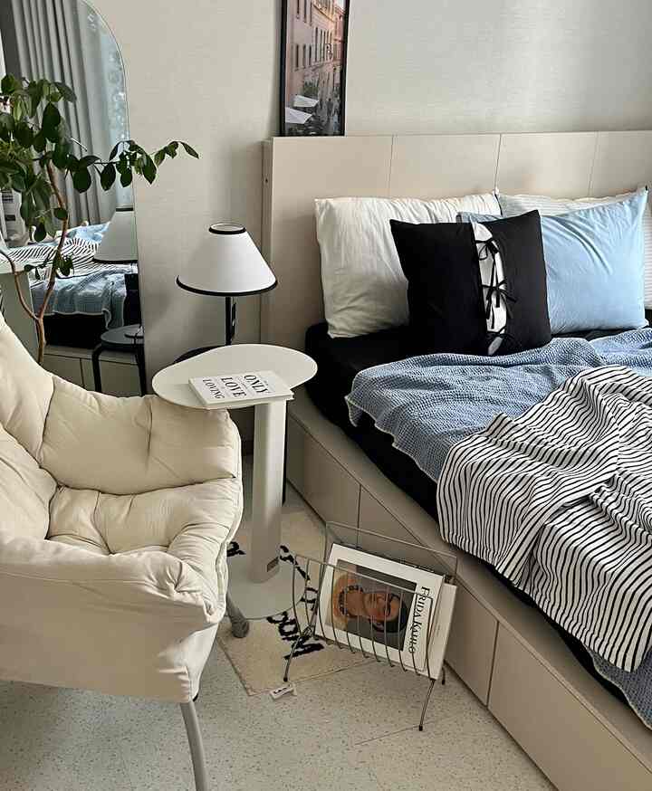 ナチュラルトーンの寝室、ベージュのアームチェアとホワイトのサイドテーブルが配置されたシンプルで落ち着いた空間